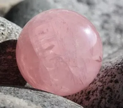 A polished rose quartz sphere rests on a textured stone surface, symbolizing love and healing.