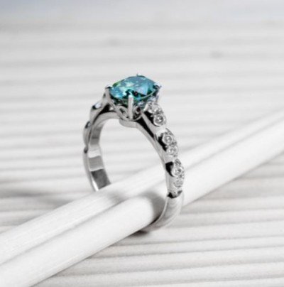 Elegant aquamarine engagement ring with detailed band and accent stones on a striped white background.